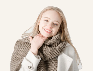 Detail view of light brown chunky knit scarf texture on white wool coat in winter