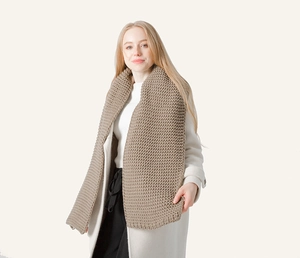 Close-up of thick knitted winter scarf in beige color showing warm wool texture