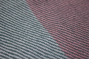 Macro shot of twill weave texture on a plaid scarf with red, grey, and black patterns