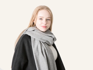 Close-up of soft grey wool scarf with fringe draped over a black coat for winter