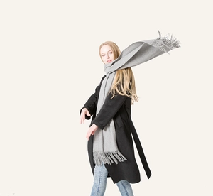 Close-up of light gray wool scarf with fringe tassels worn over a long black wool coat