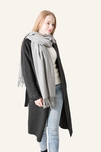 Close-up of light grey wool scarf with long tassels paired with a long black winter coat
