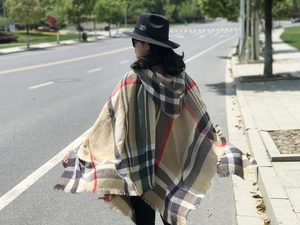 Scatto all'aperto di un classico poncho scozzese con cappuccio e nappe in finto cashmere