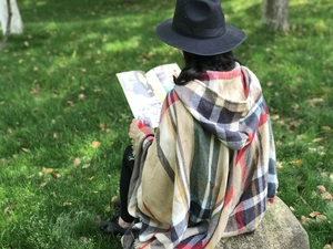 Scatto all'aperto di un poncho con cappuccio a quadri beige con nappine e dettagli frange