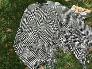 Detail of black and white houndstooth poncho fabric texture with tassel fringe edges