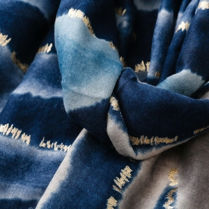 Detail aus blauem Tie-Dye-Stoff mit Goldfolienakzenten und weichen Fransen am Rand