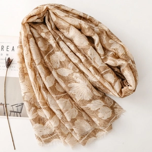 Detail of floral print scarf with gold foil accents and soft frayed edges on beige fabric