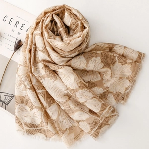 Detailed texture of champagne gold scarf with white ginkgo leaf patterns and frayed edges