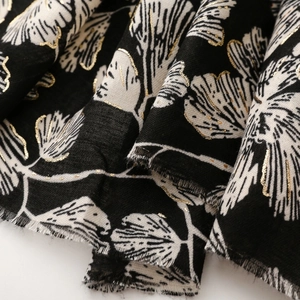 Detailed macro of floral pattern on cotton-linen scarf with gold foil accents and frayed edges