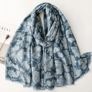 Macro detail of silver ginkgo leaf print on soft grey-blue scarf with raw tassel edges