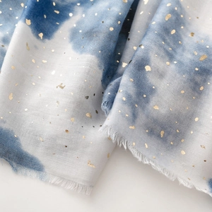 Detail of blue tie-dye scarf with gold foil accents and soft frayed tassel edges