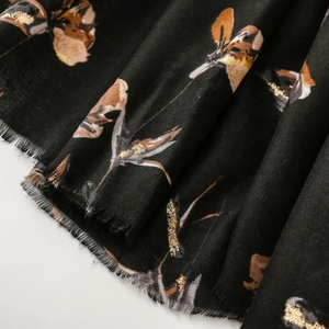 Macro shot of cotton linen scarf detail featuring gold floral print and fringe tassels