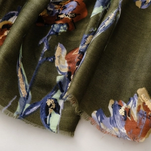Close-up of olive green cotton-linen scarf with floral prints and gold foil details