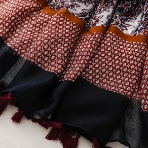 Close-up of bohemian linen shawl featuring red paisley prints and dark fringe tassels