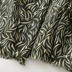 Close-up of green cotton linen scarf with gold foil accents and frayed tassel edges