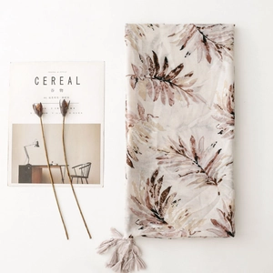 Elegant off-white scarf with brown leaf print and tassel trim on minimalist magazine background