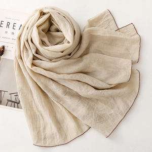 Detail eines beigen Leinenschals mit feiner brauner Kontrastnaht und Knitterstruktur