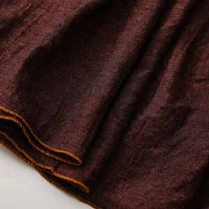 Nahaufnahme von weinrotem Leinenstoff mit präziser orangefarbener Overlock-Naht