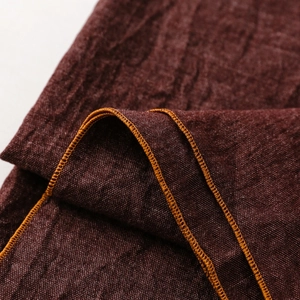 Detail eines dunkelbraunen Leinenschals mit Naturstruktur und orangefarbenen Nähten