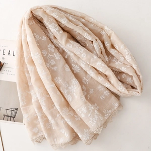 Close-up of beige linen scarf featuring white floral embroidery and delicate lace edges