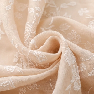 Close-up of light beige linen scarf featuring delicate white floral embroidery details