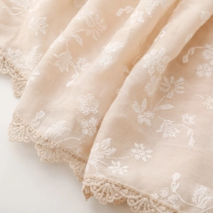 Close-up of cream cotton linen scarf featuring white floral embroidery and lace trim