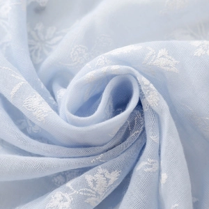 Detail of light blue fabric featuring white floral embroidery and breathable texture