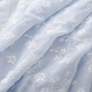 Macro shot of light blue cotton-linen fabric with delicate white floral embroidery details