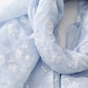Close-up of light blue cotton scarf with white floral embroidery and delicate texture