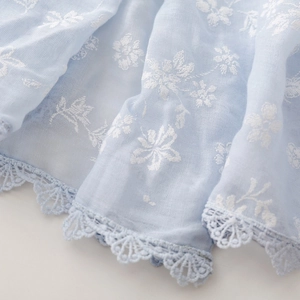 Detailed close-up of light blue cotton linen scarf with white floral embroidery and lace trim
