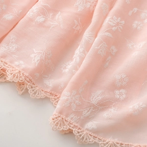 Detailed macro view of white floral embroidery and crochet lace on soft pink fabric
