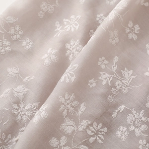 Detailed macro view of delicate white floral embroidery on a soft beige linen scarf