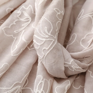 Dettaglio del morbido tessuto beige in cotone e lino con eleganti ricami floreali bianchi