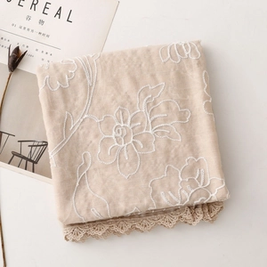 Dettaglio sciarpa di cotone beige con ricami floreali bianchi e pizzo delicato