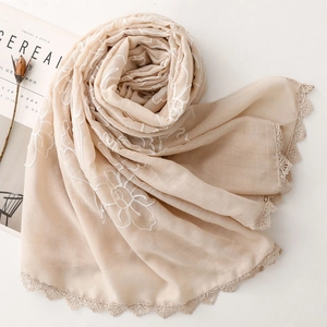 Dettaglio di ricami e bordi in pizzo su una sciarpa beige in cotone-lino con fiori