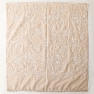 Dettaglio del ricamo floreale e bordi in pizzo su una sciarpa beige in cotone-lino