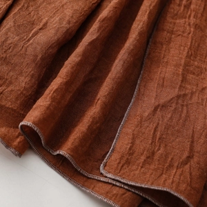 Detail aus rostbraunem Baumwollleinen mit natürlicher Knitteroptik und sauberer Randnaht