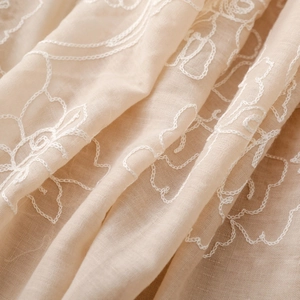 Dettaglio di elegante sciarpa beige in cotone e lino con delicati ricami floreali bianchi