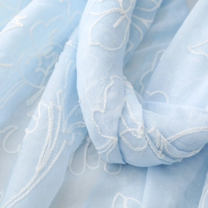 Dettaglio ravvicinato di una sciarpa in cotone-lino azzurro con elegante ricamo di fiori bianchi