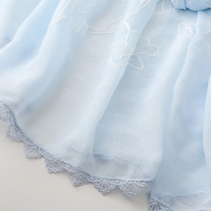 Dettaglio di sciarpa in cotone azzurro con ricamo floreale bianco e bordo in pizzo