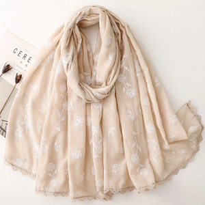 Détail d'une écharpe crème avec broderie de roses blanches et bordure en dentelle