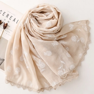 Gros plan d'une écharpe beige avec broderie de roses blanches et bordure en dentelle