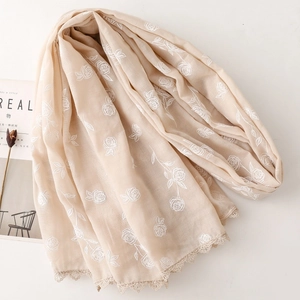 Détail d'une écharpe beige avec broderie de roses blanches et bordures en dentelle