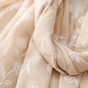 Gros plan d'une broderie de roses blanches sur une écharpe beige en coton et lin doux