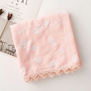Détail d'une écharpe rose corail avec broderie de roses et bordure en dentelle