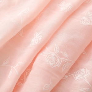 Détail macro d'une écharpe rose clair avec broderie de roses blanches et tissu doux