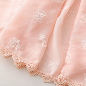 Détail d'une écharpe en coton rose avec broderie de rose blanche et bordure en dentelle