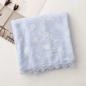 Détail de l'écharpe bleu clair avec broderie de roses blanches et bordure en dentelle