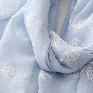 Gros plan d'une écharpe bleu clair en coton et lin avec broderie florale de roses blanches
