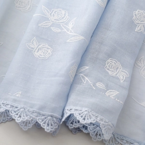 Détail de l'écharpe en coton et lin bleu clair avec broderie rose et dentelle